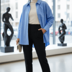 Femme élégante portant une chemise oversize rayée bleu clair avec un col roulé crème et un pantalon noir dans un cadre moderne