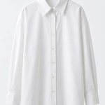 Chemise blanche classique pour femme avec coupe oversize, présentée sur un cintre, style minimaliste et élégant.