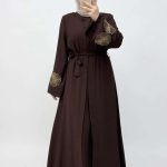 Femme portant une abaya marron élégante avec des broderies florales sur les manches, collection Orkidia Fashion.
