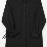 Chemise noire élégante à manches longues avec détails de volants et liens à nouer, vue de face sur fond clair.
