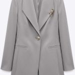 Blazer gris cintré élégant avec broche chaîne dorée, parfait pour une tenue professionnelle femme.