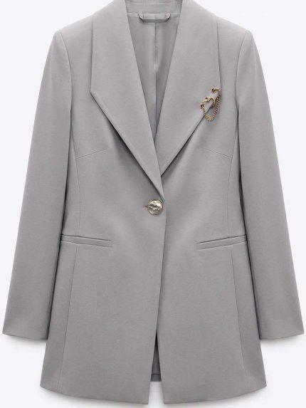 Blazer gris cintré élégant avec broche chaîne dorée, parfait pour une tenue professionnelle femme.