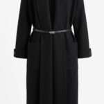Manteau long noir en maille avec ceinture fine et poches plaquées, style minimaliste et élégant.